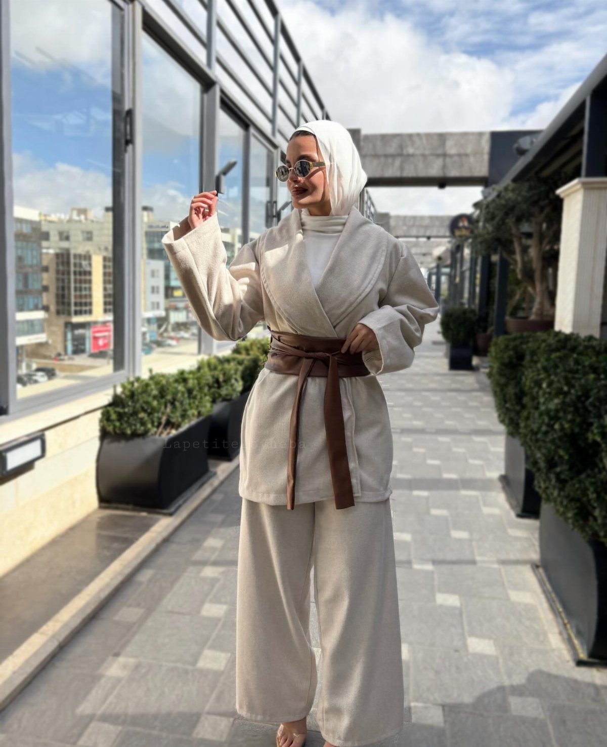 Woman in beige wrap jacket and wide-leg trousers with a brown leather belt.