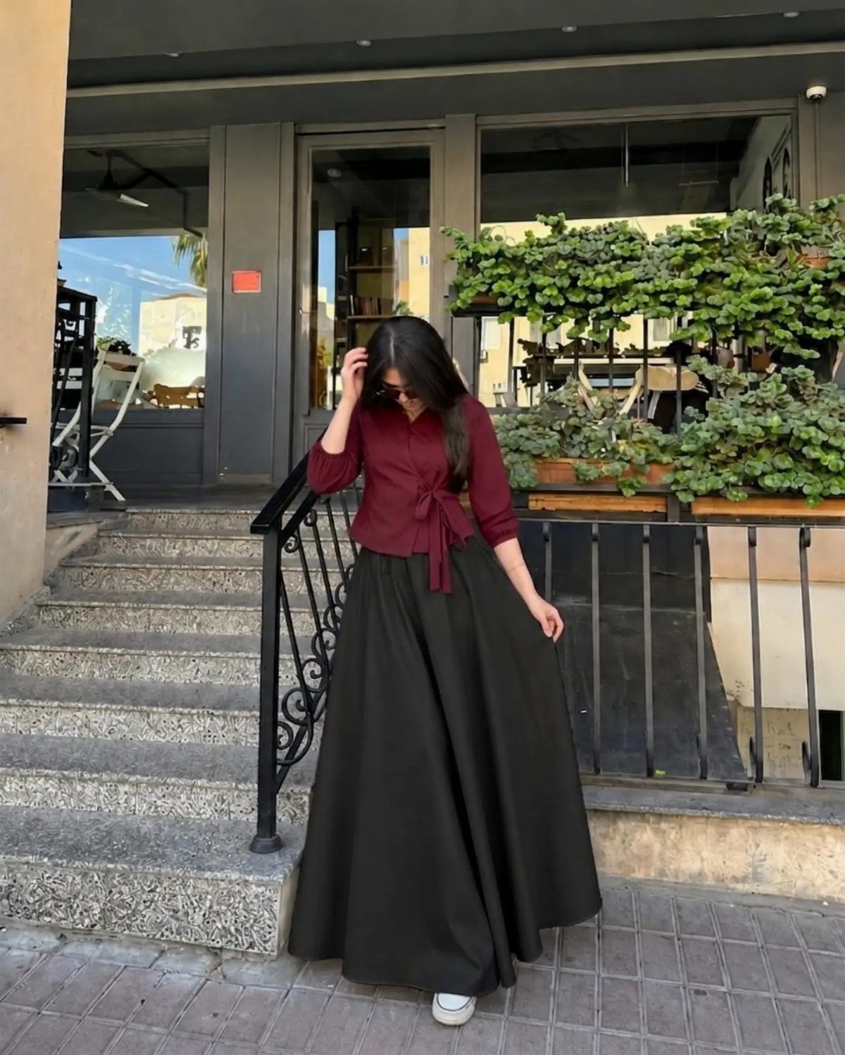 Woman wearing a maroon button-up shirt and a long black flowing maxi skirt.