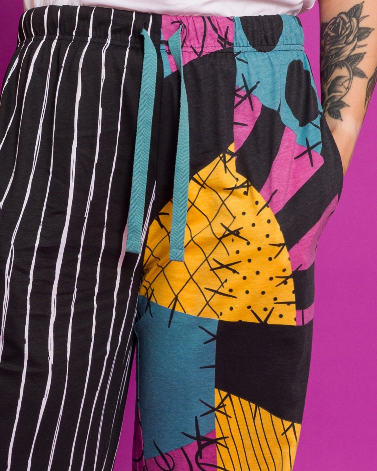 Colorful patchwork and striped pajama pants worn by a person against pink background