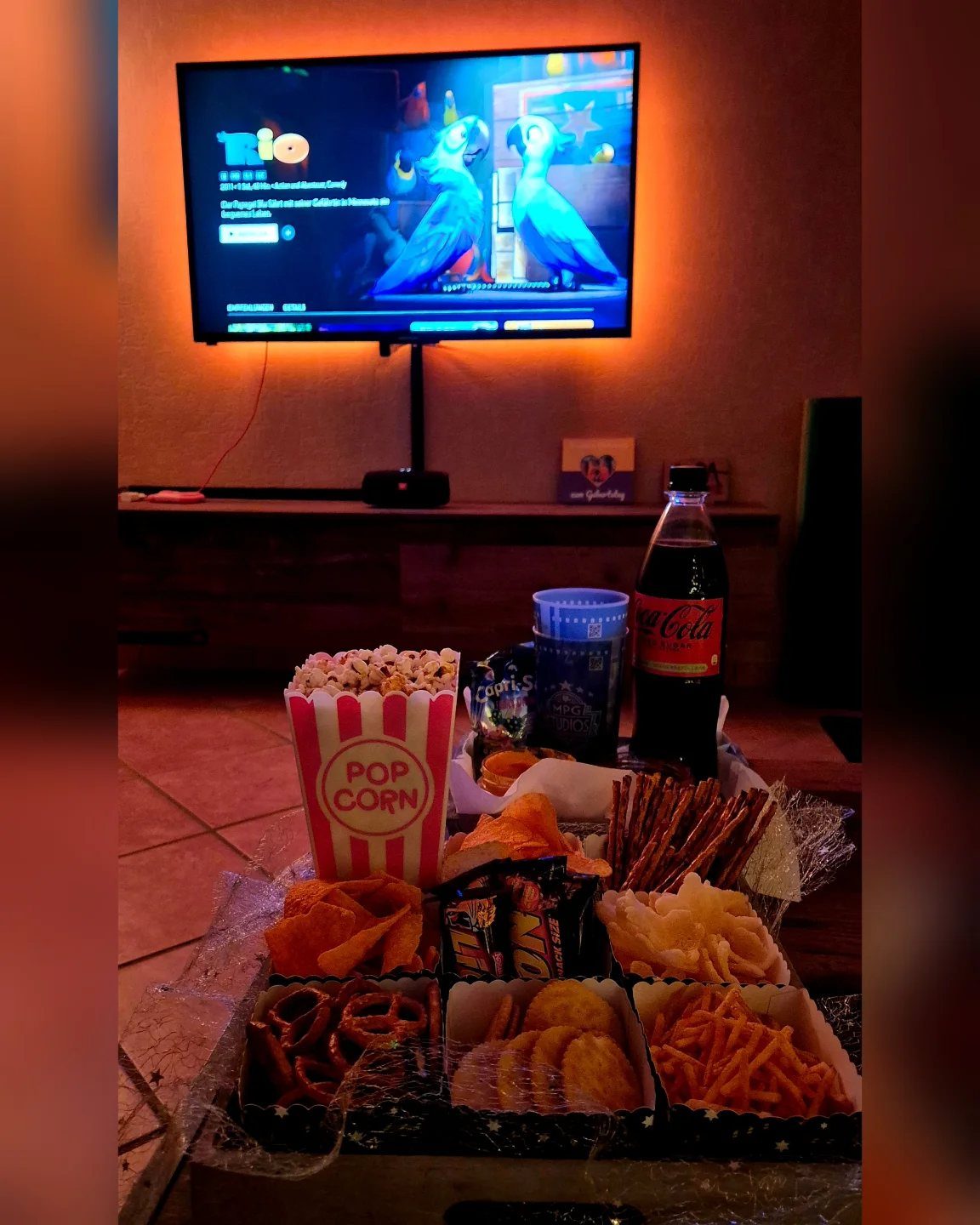 Movie snacks including popcorn and soda arranged in front of a television screen.