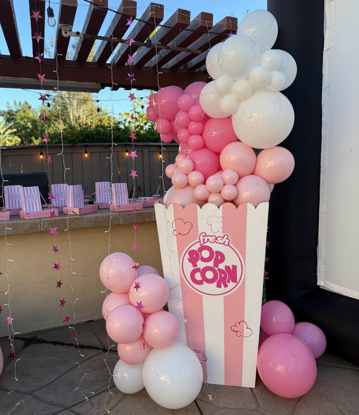 Popcorn bucket prop with pink and white balloons at a movie themed party.