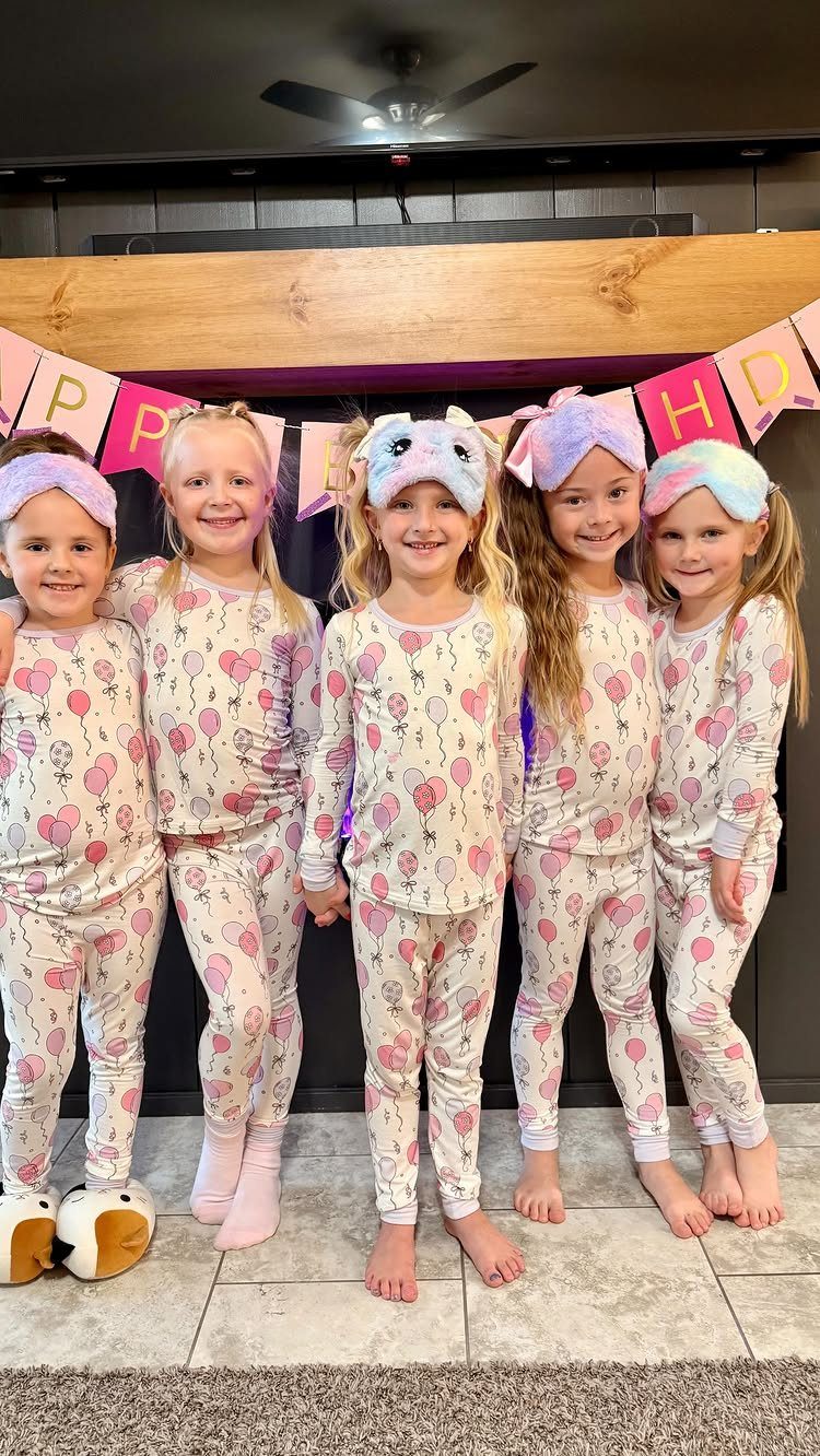 Five young girls in matching balloon pajamas posing under a birthday banner.