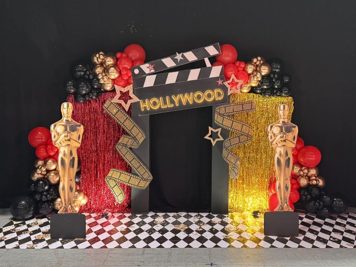 Movie themed photo booth with gold statues, balloons, and Hollywood clapperboard sign.