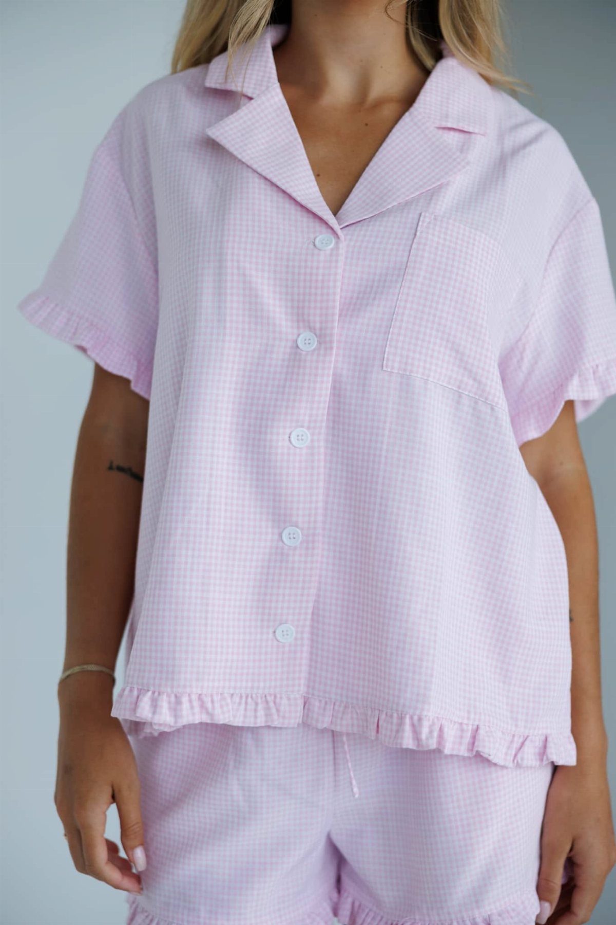 Person wearing a light pink and white gingham print pajama set with ruffles.