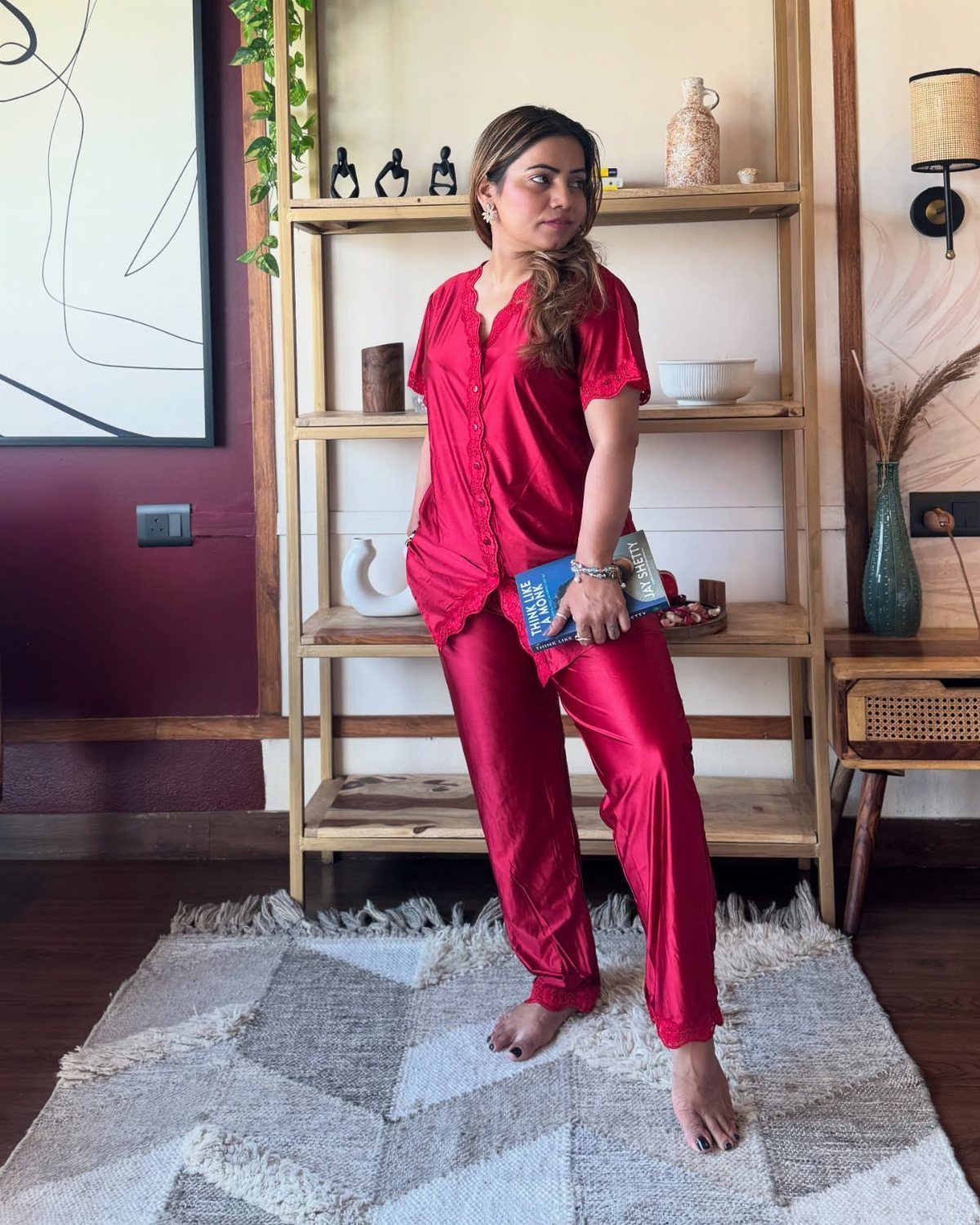 Woman wearing red satin pajama set standing on a patterned rug indoors.
