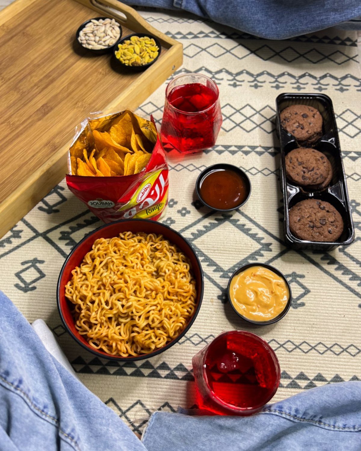 Assorted snacks including noodles, chips, and chocolate chip cookies on a patterned rug.