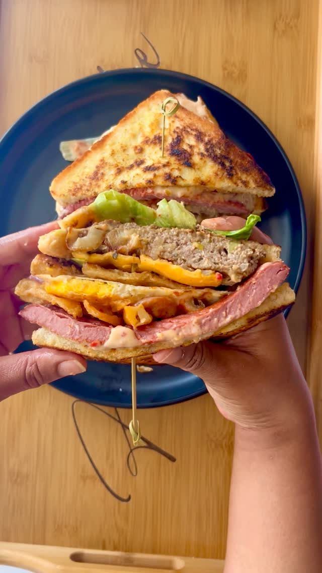 Towering multi-layered sandwich with meat and cheese held by two hands.