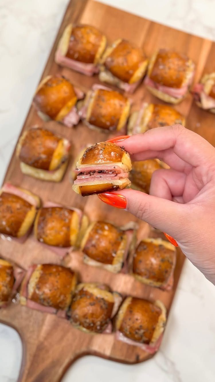 Small ham and cheese sliders on a wooden board held by a hand.