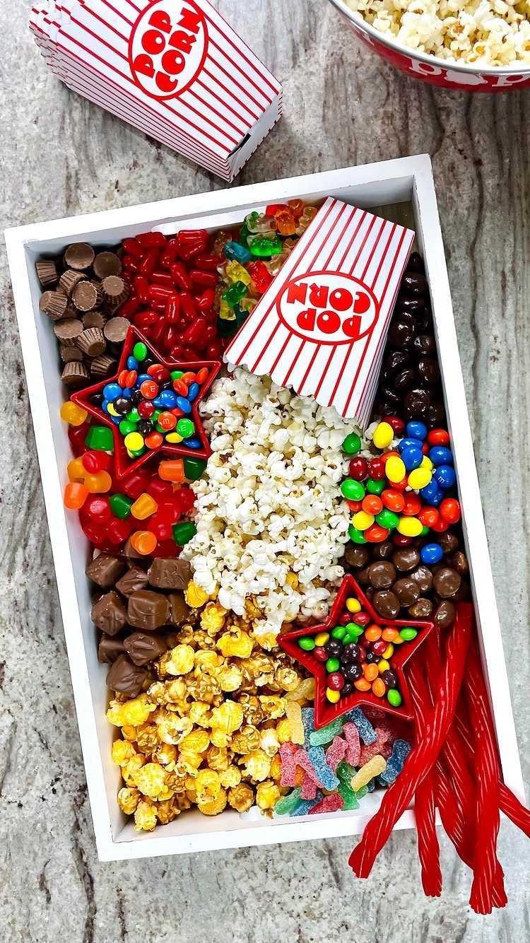 Movie snack tray with popcorn, assorted candies, and red-and-white striped popcorn boxes.