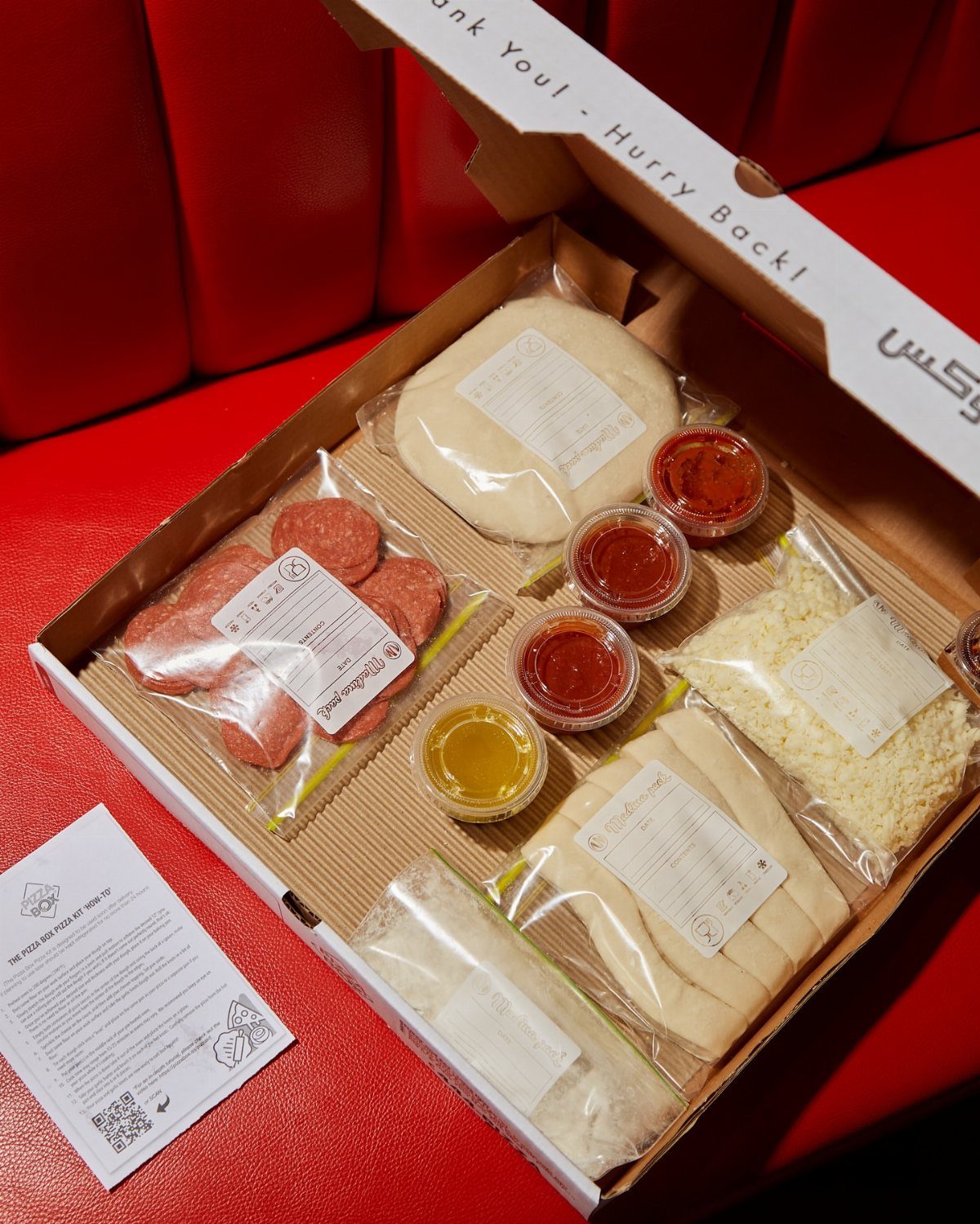 Pizza kit in a cardboard box with dough, cheese, pepperoni, and sauce.