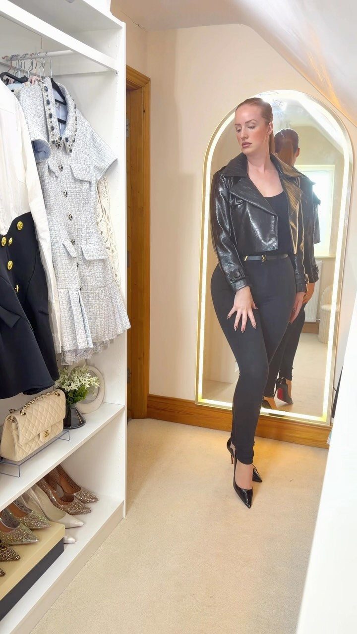 Woman wearing an all-black ensemble with a leather jacket in a white closet.