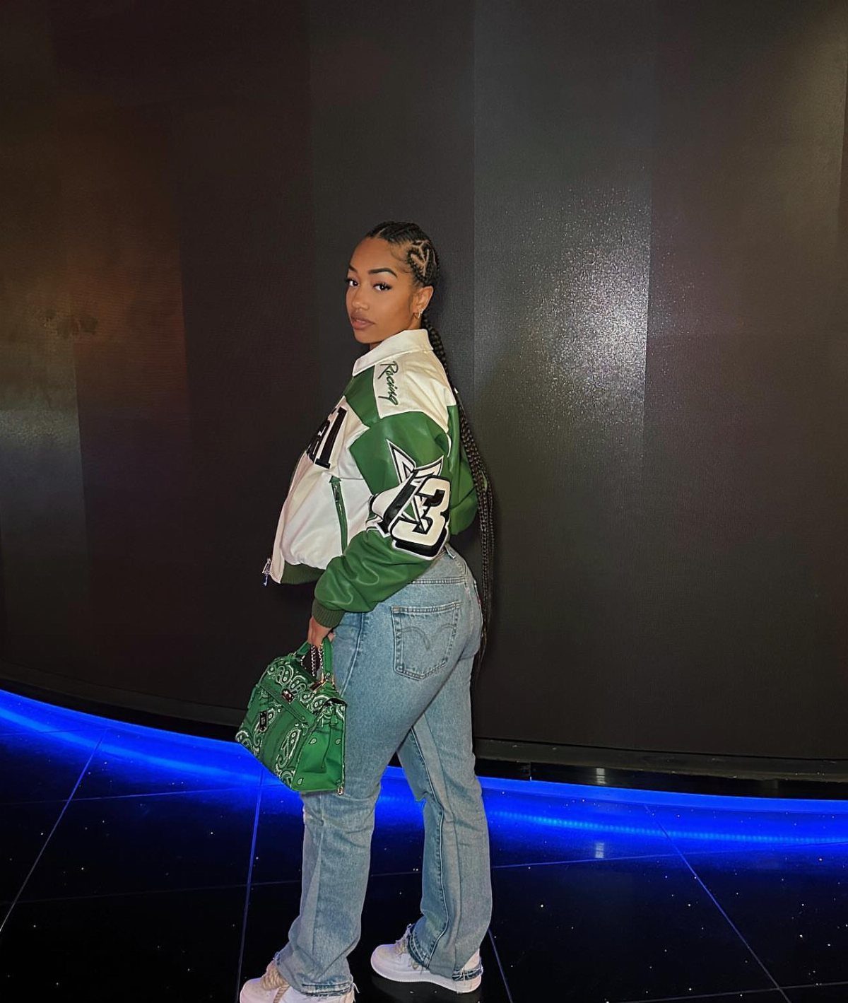 Woman wearing a green and white bomber jacket with light-wash blue jeans.