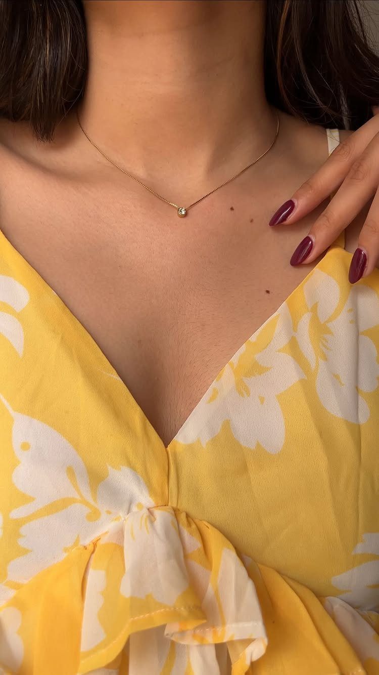 Thin gold chain necklace with a small pendant worn with yellow floral dress