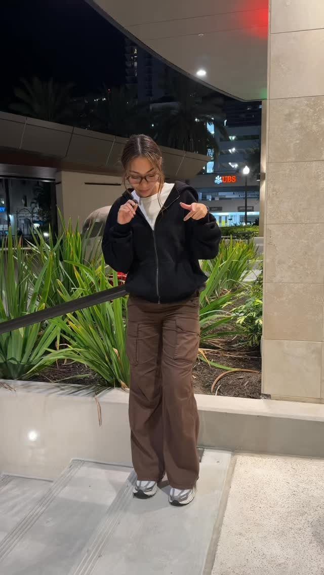 Woman wearing a black hoodie over a white shirt and brown cargo pants.