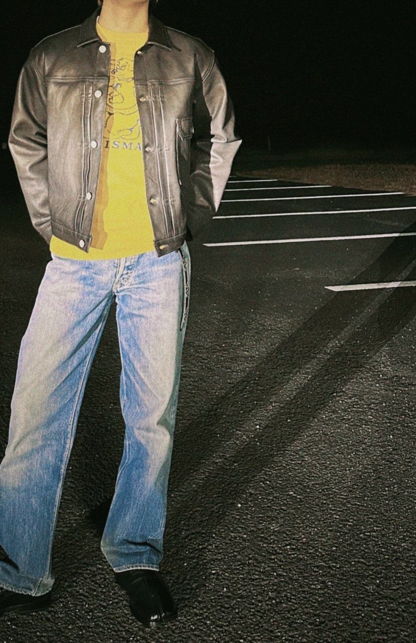 Person wearing a black leather jacket, yellow graphic tee, and light blue jeans.