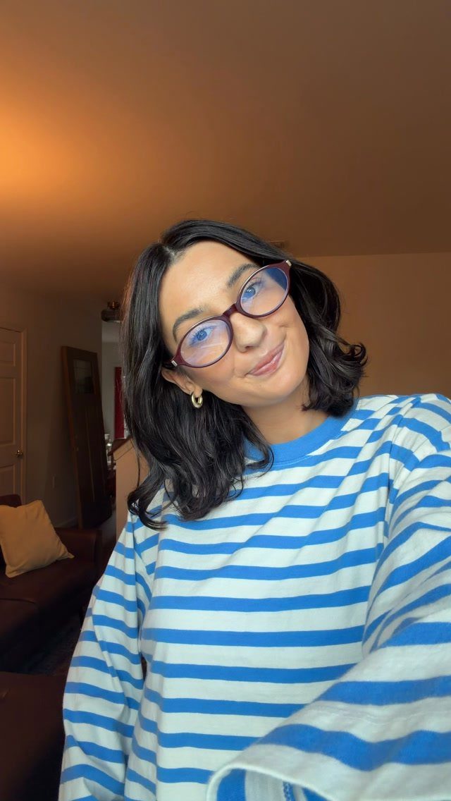 Woman wearing a blue and white striped oversized sweater and glasses indoors.