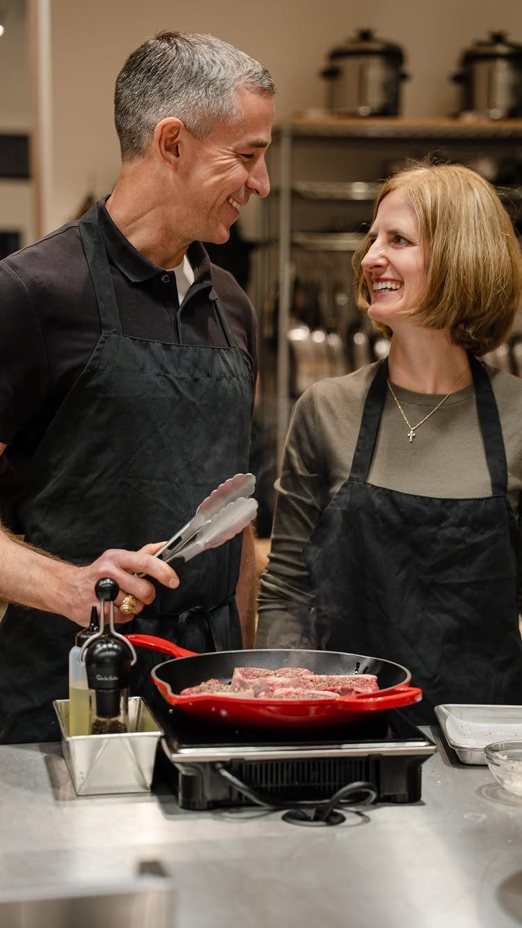 Man and woman in black aprons cooking meat together in a professional kitchen.