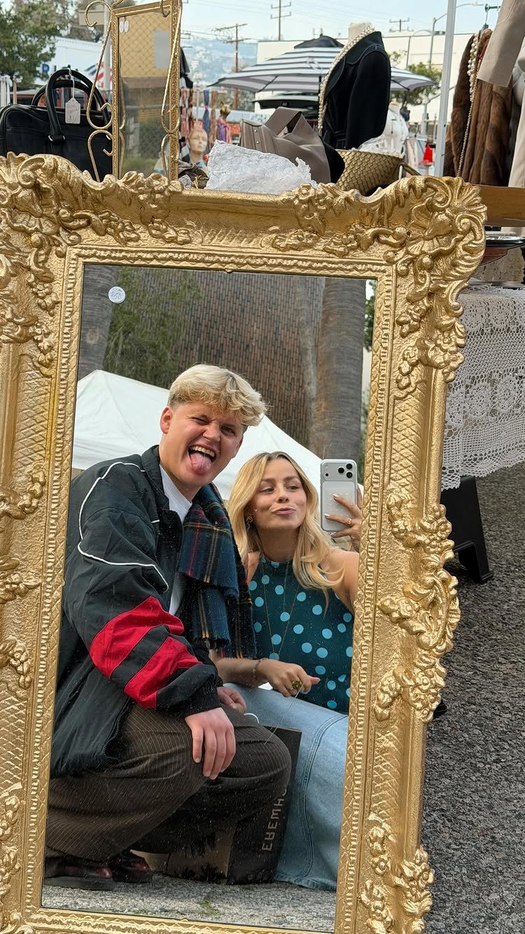 Young couple taking a mirror selfie in a gold frame at a flea market