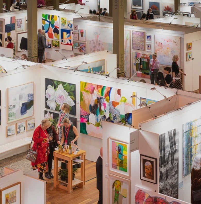 Art fair with colorful paintings displayed in white booths and people browsing.