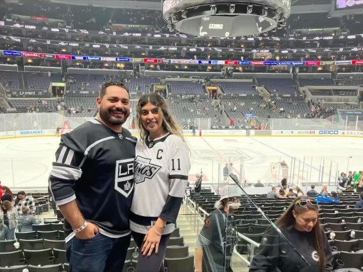 Couple wearing LA Kings jerseys posing in a large ice hockey arena.