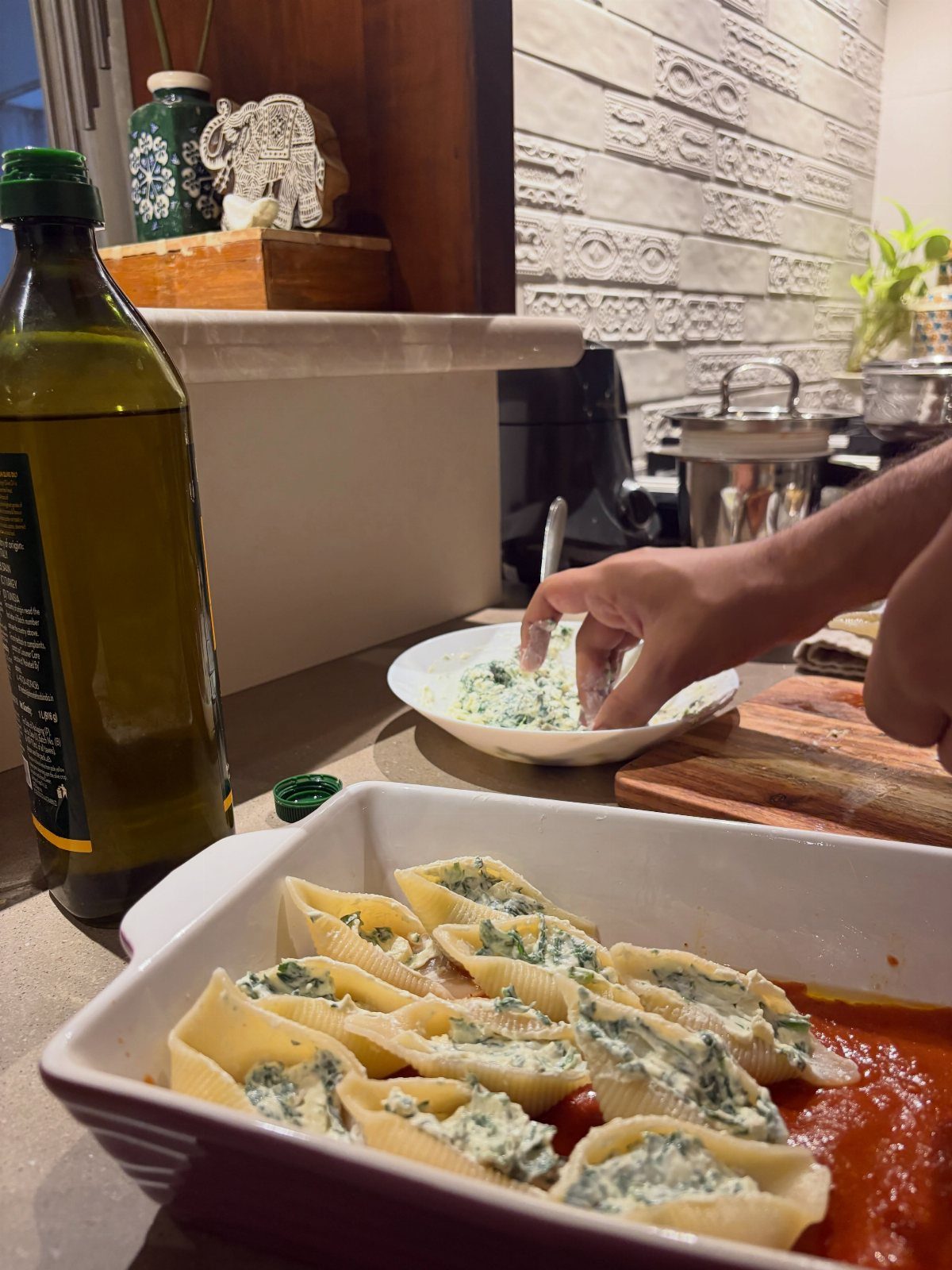 Hand filling pasta shells with ricotta spinach mixture in a baking dish