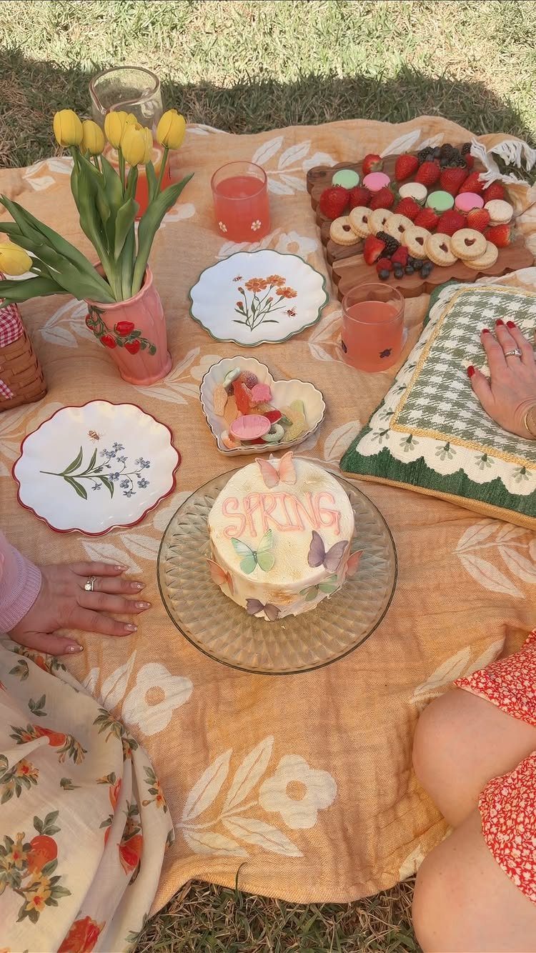 Picnic spread with a spring cake, fruit platter, and yellow tulips on grass.