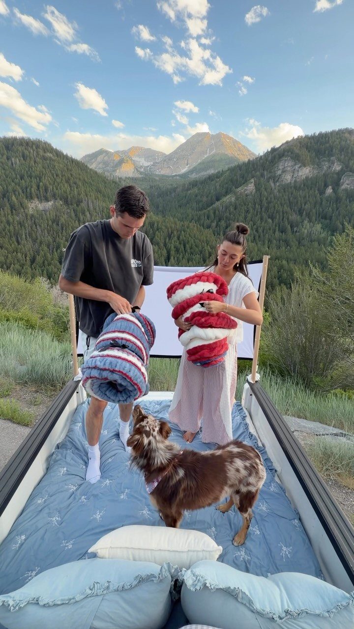 Couple and their dog in a truck bed lounge overlooking scenic green mountains.