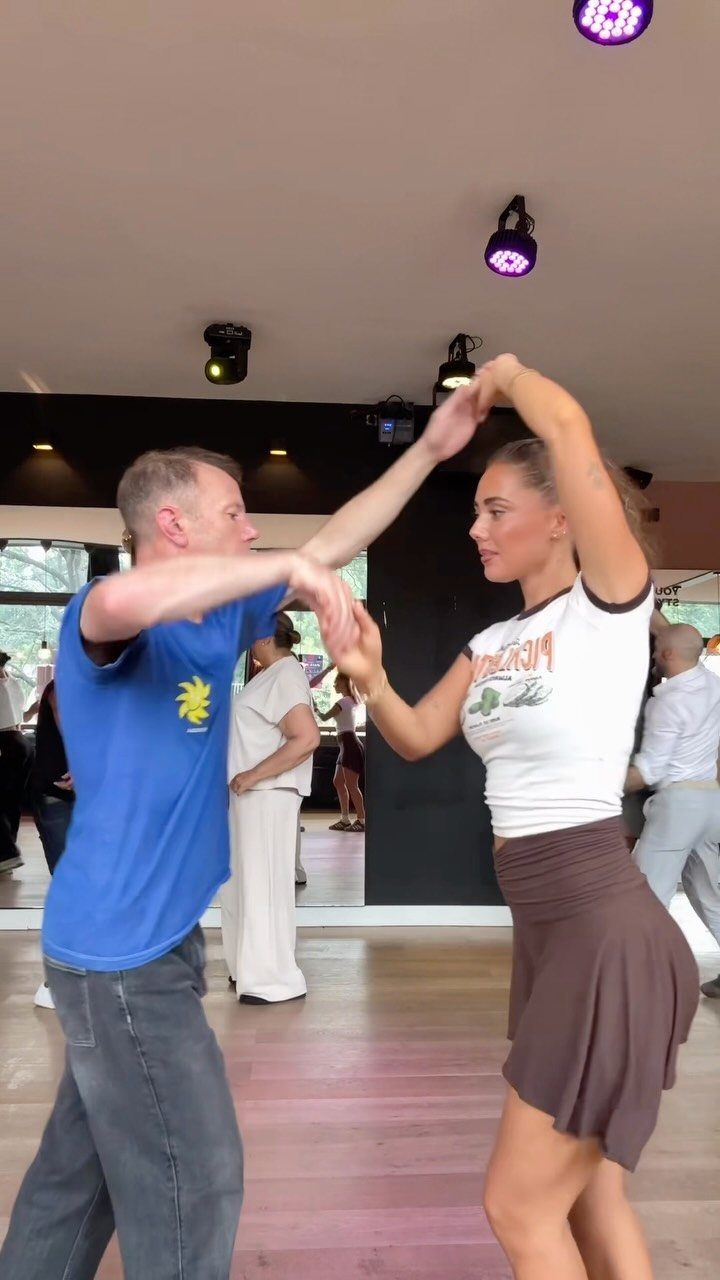 A man and woman dancing together in a studio with purple lighting.