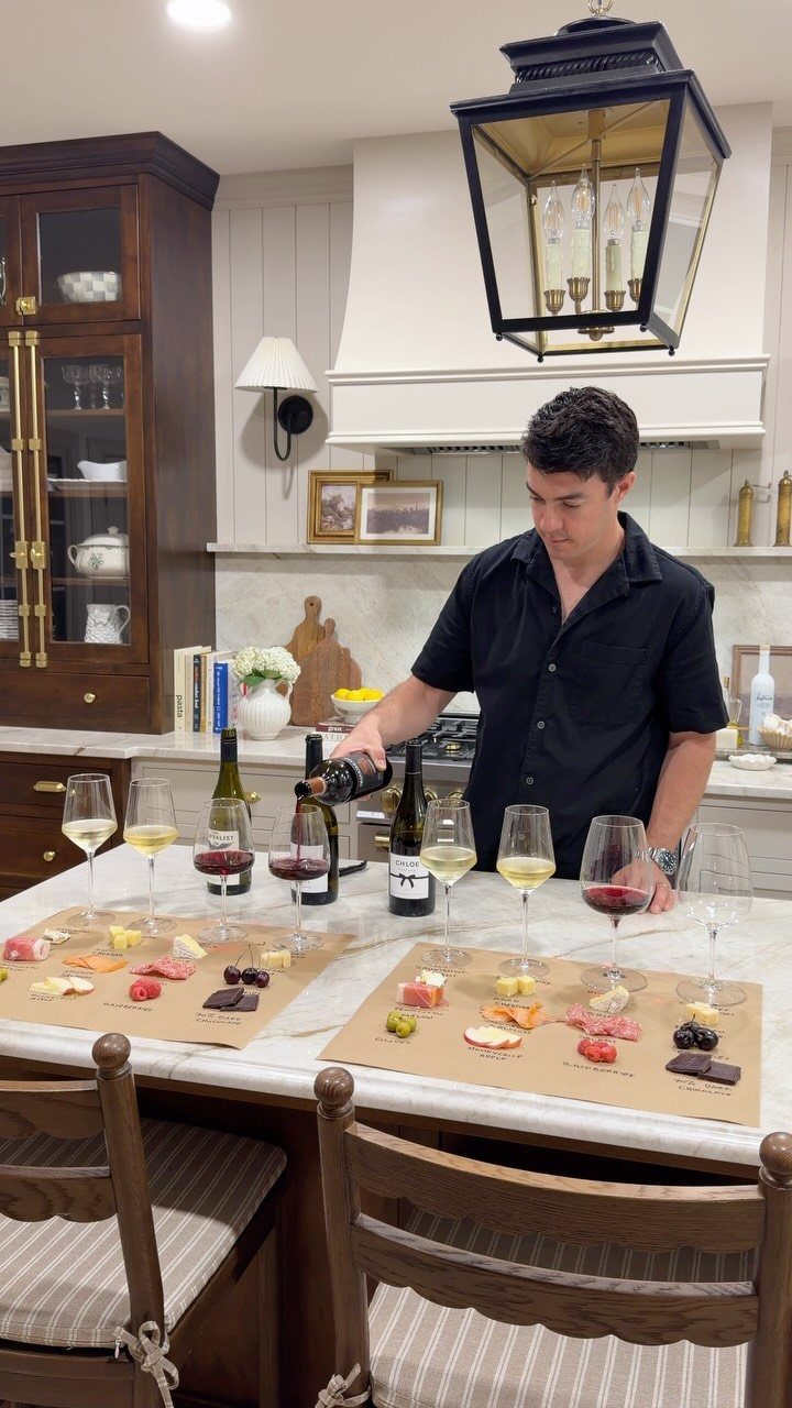 Man pouring red wine next to charcuterie boards on a white kitchen island