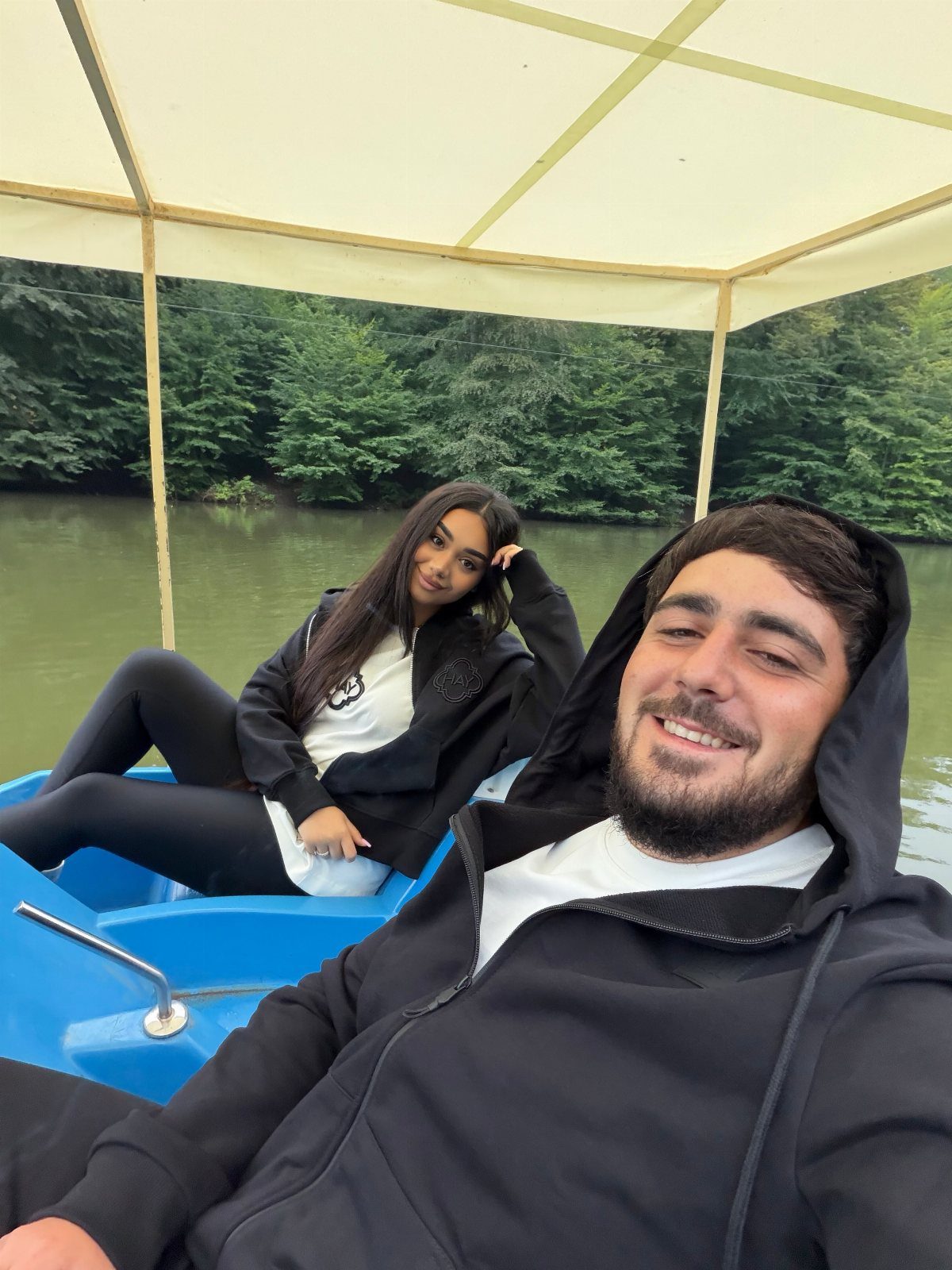 Couple in black hoodies relaxing in a blue boat on a river.