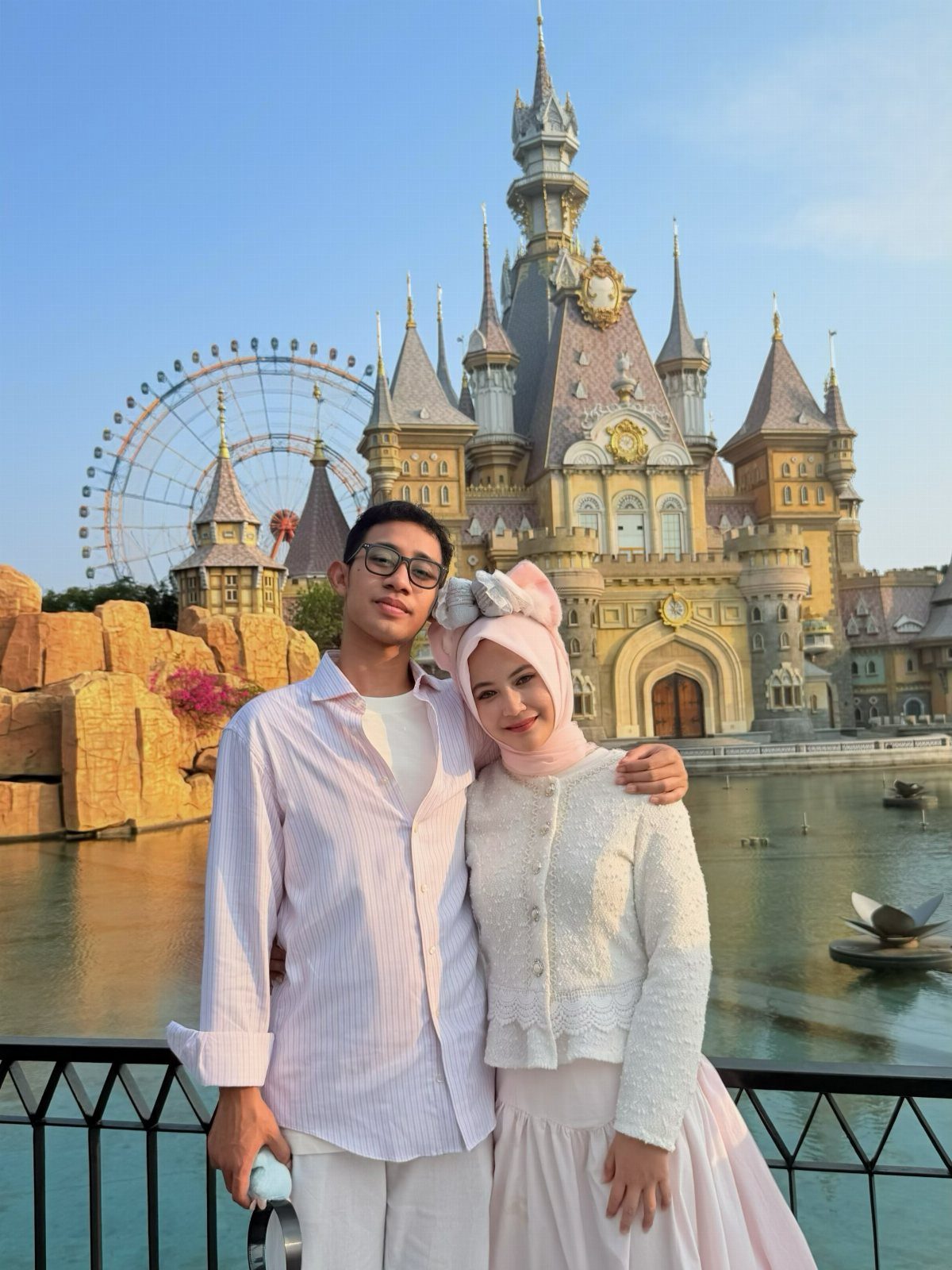 Couple posing in front of a fairytale castle and Ferris wheel at an amusement park.
