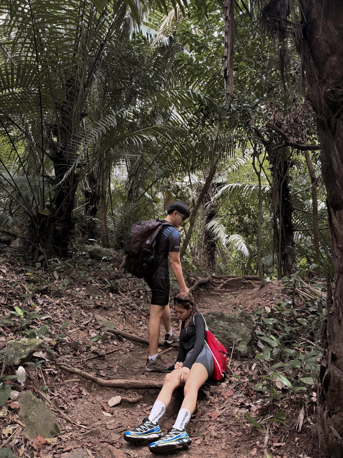 Couple hiking on a dirt trail surrounded by lush green forest trees.