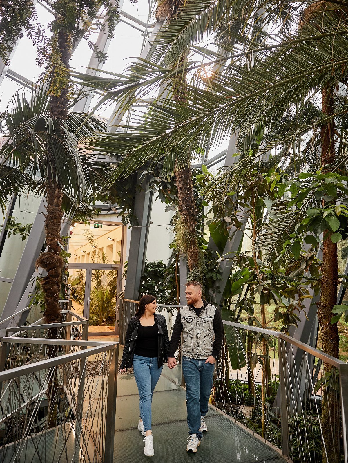 Couple holding hands while walking through a lush glass botanical garden conservatory.