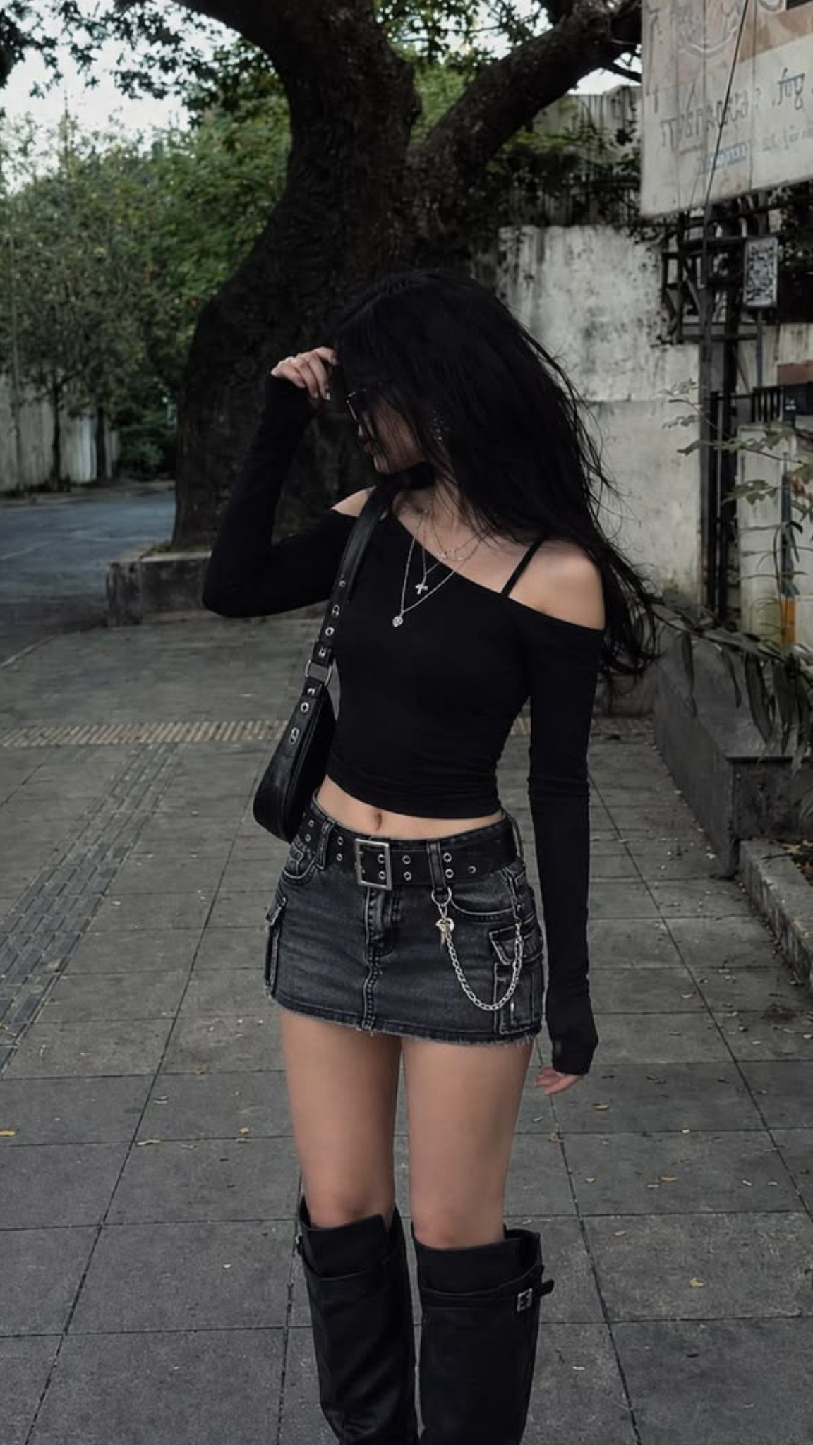 Woman in black off-the-shoulder top, denim mini skirt, and knee-high boots on street.