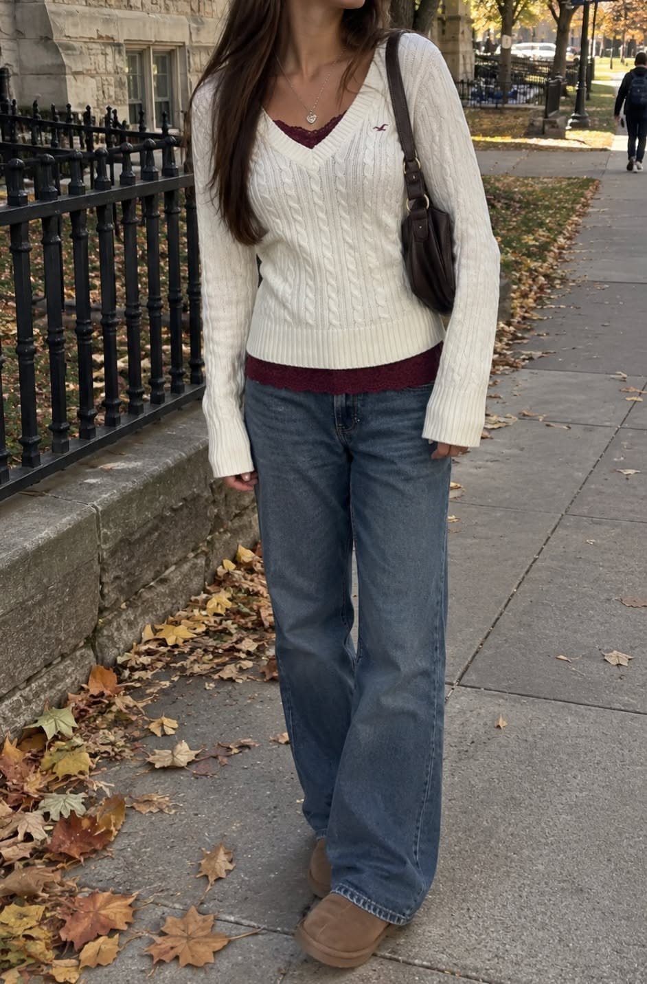 Person wearing a white cable-knit sweater over a maroon shirt and wide-leg jeans.