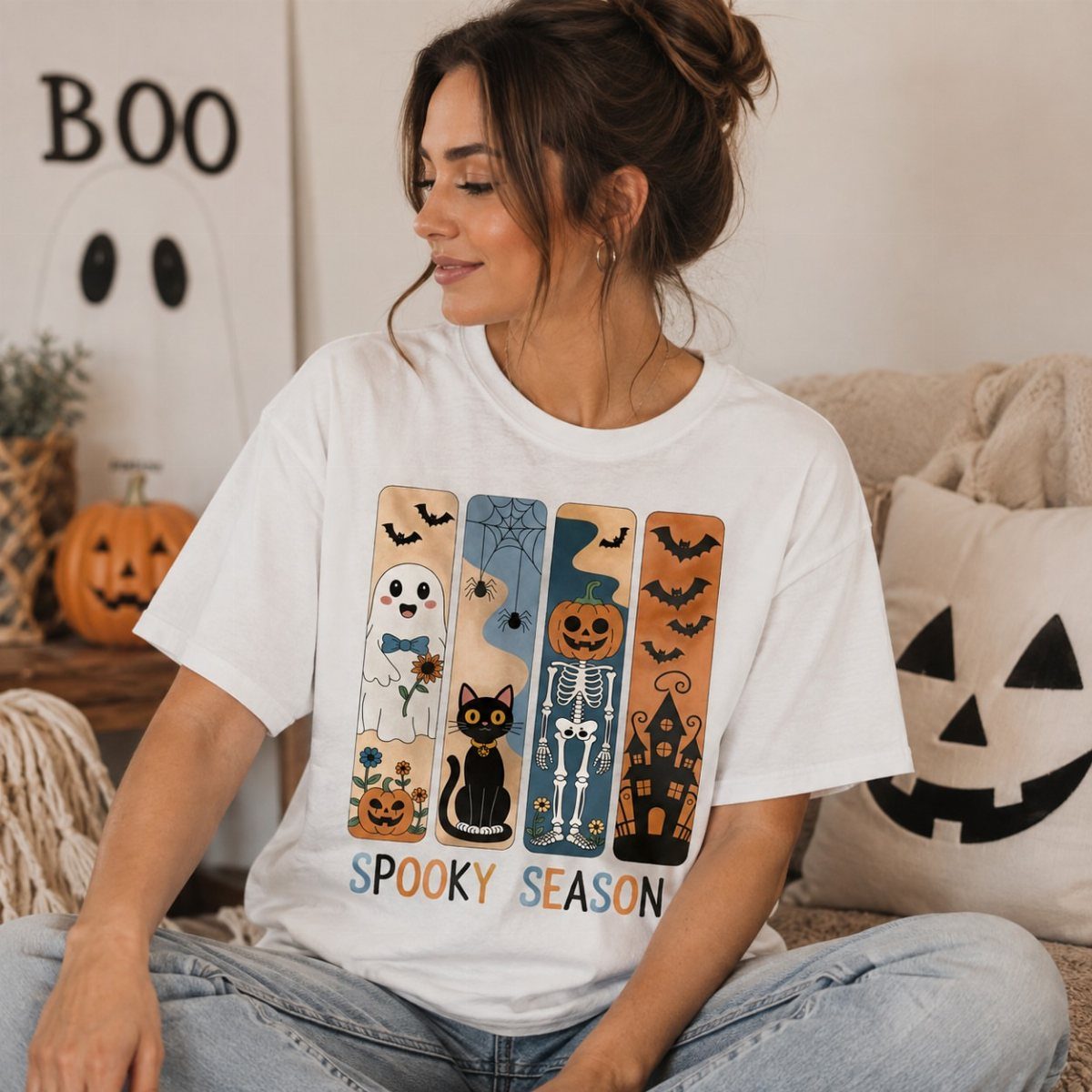 Woman wearing a Halloween graphic tee and light blue jeans sitting among pumpkins.