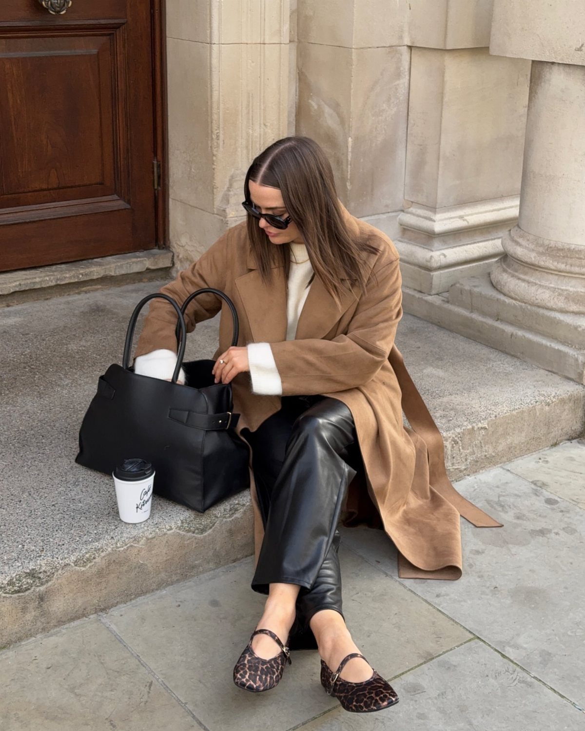 Woman in tan coat, cream jumper, black leather trousers, and leopard print slingbacks.