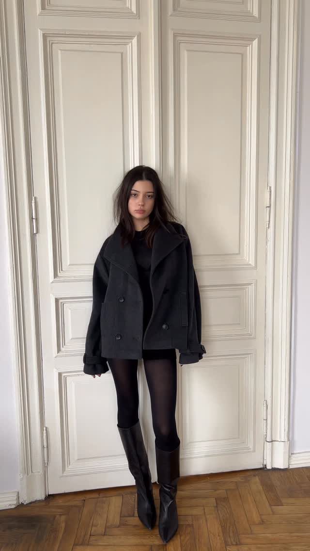 Woman in an oversized grey wool coat, black tights, and brown leather boots.