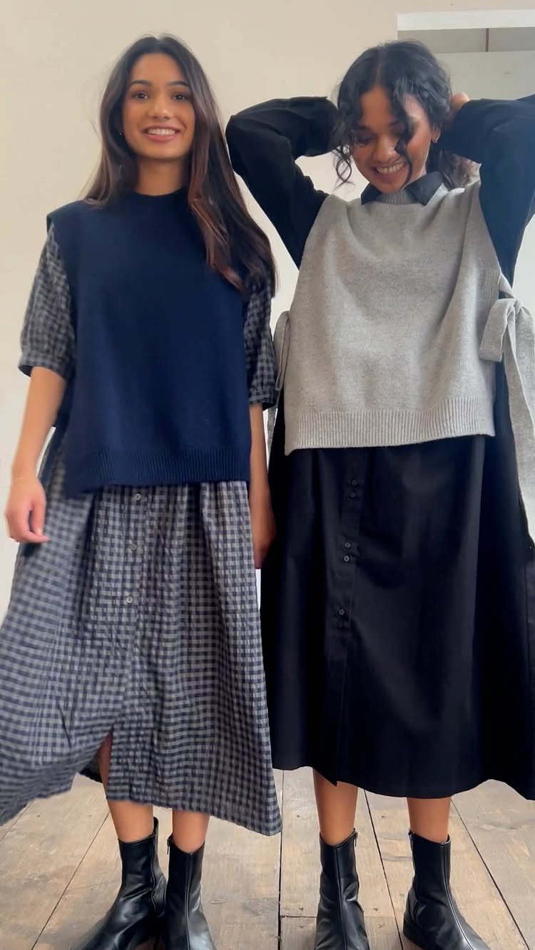 Two women wearing sweater vests over midi dresses and black ankle boots.