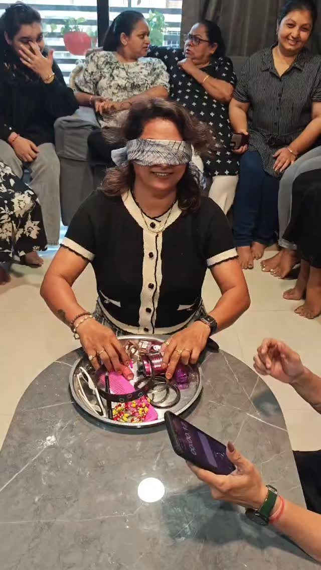 Blindfolded woman reaching for objects on a tray while friends watch her.