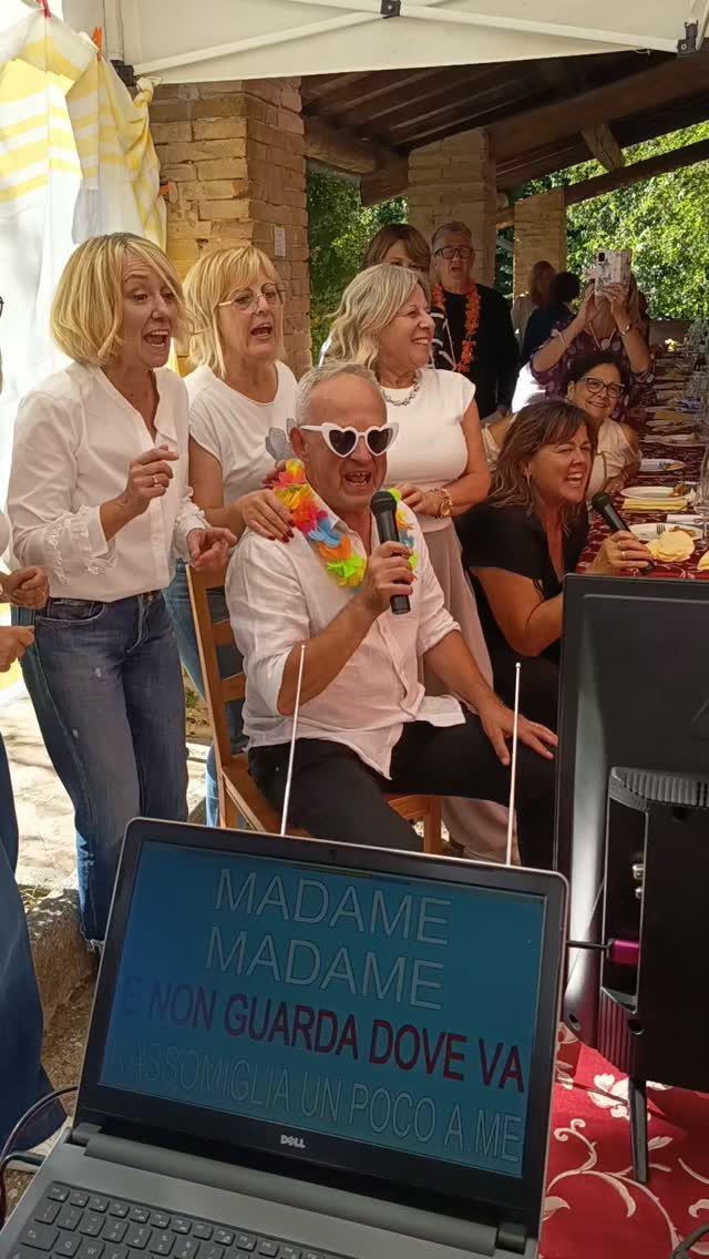 Group of adults singing karaoke outdoors with a laptop displaying lyrics in foreground