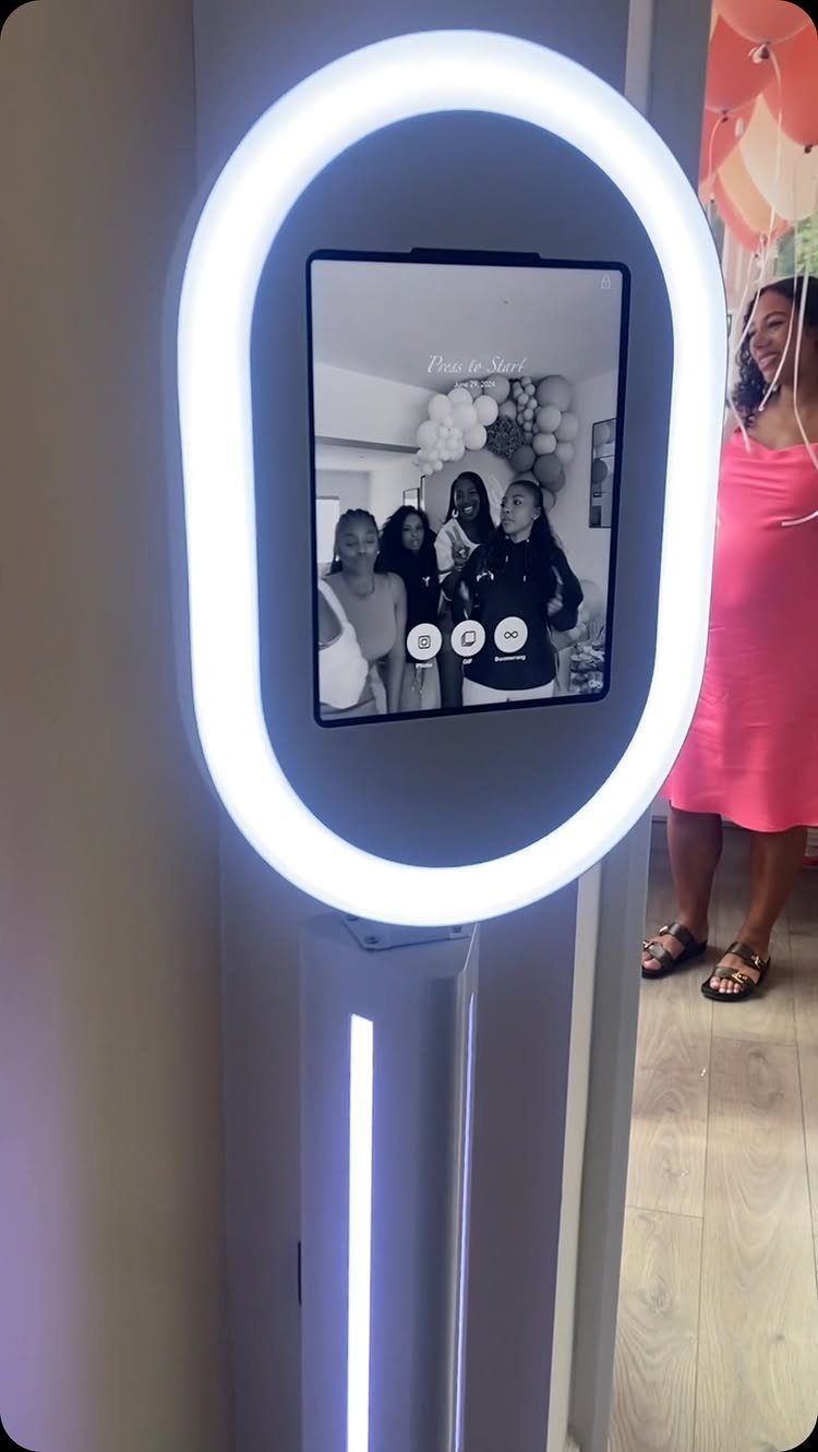 Digital photo booth kiosk with a bright ring light and screen showing guests.