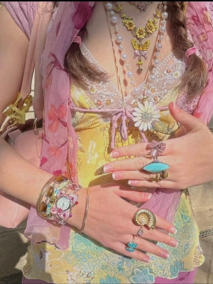 Person wearing a colorful layered outfit with yellow dress, pink wrap, and jewelry.