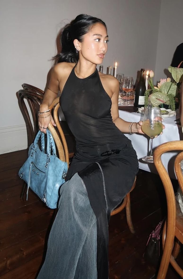 Woman in black halter dress and grey trousers holding wine at dinner party