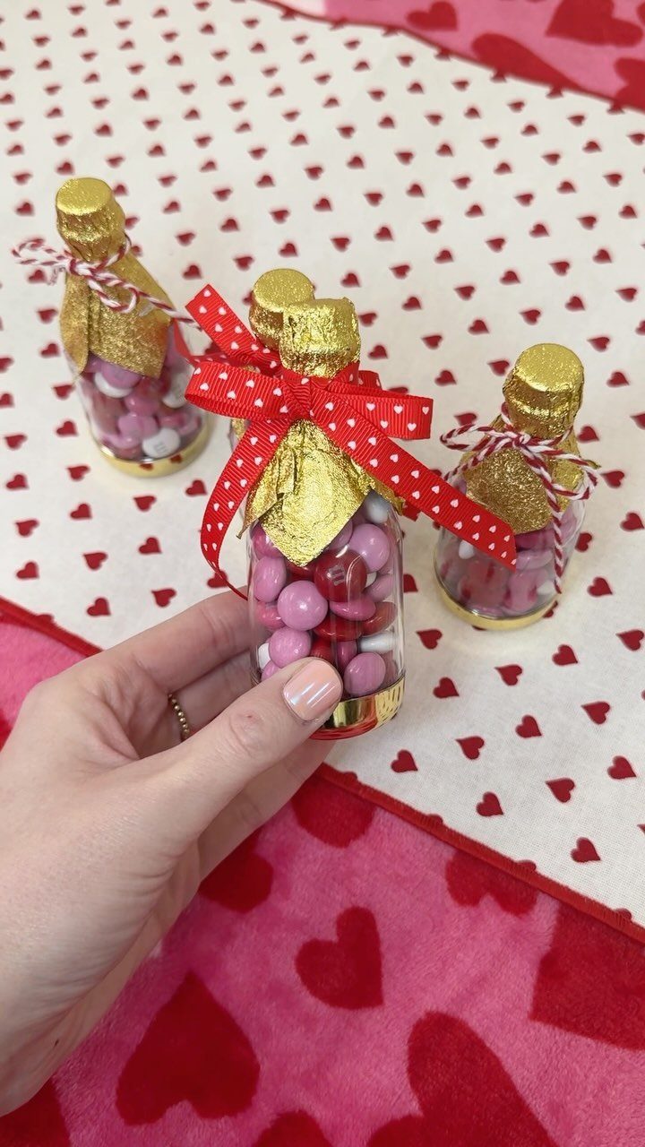 Small glass bottles filled with pink candies and red bows on heart-patterned fabric.