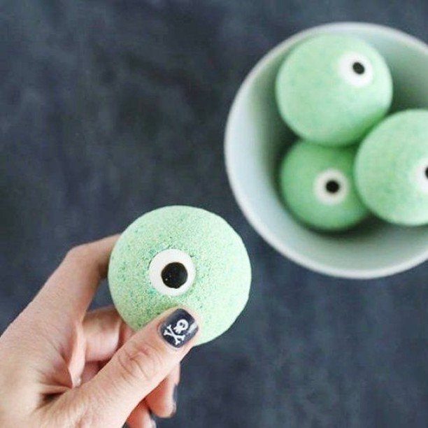 Green eyeball-shaped bath bombs, one held by a hand and others in a bowl.