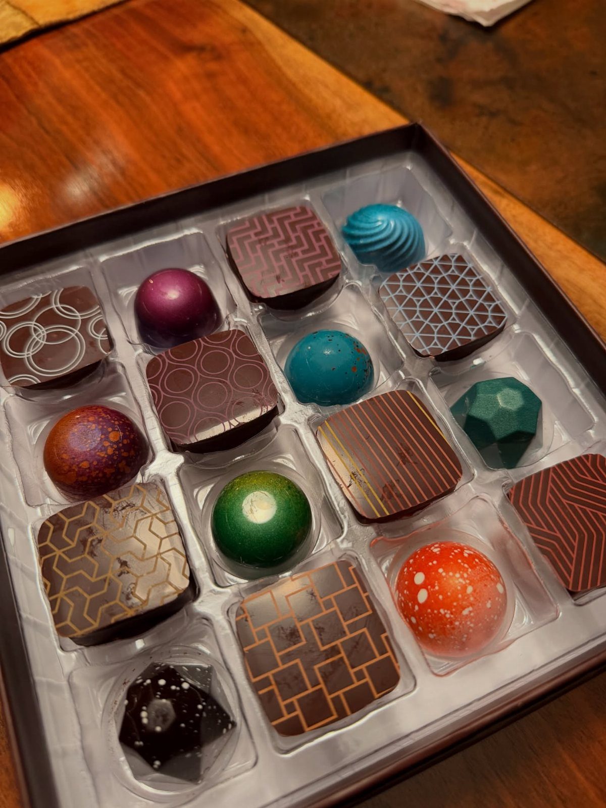 Assorted gourmet chocolates in colorful shapes and patterns inside a black gift box.
