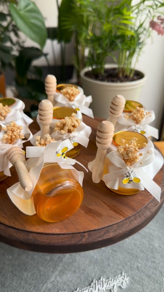 Small honey jars with wooden dippers and white ribbons on a wooden platter