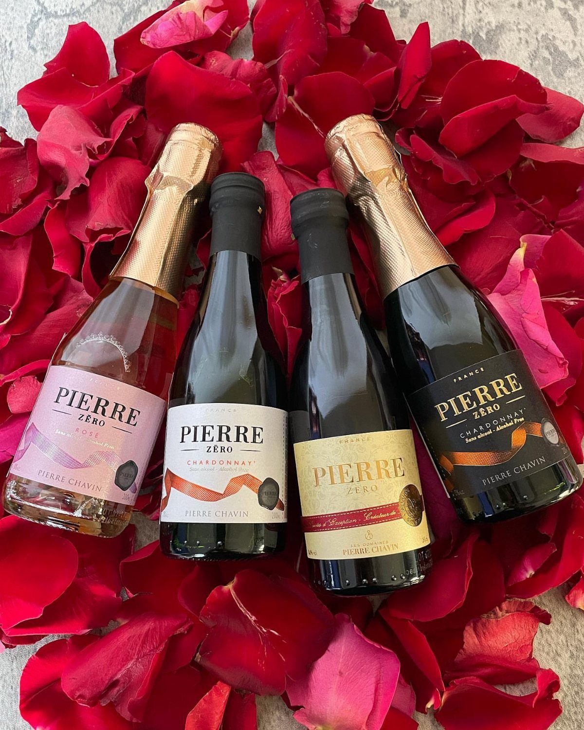Four mini bottles of wine and champagne resting on red rose petals