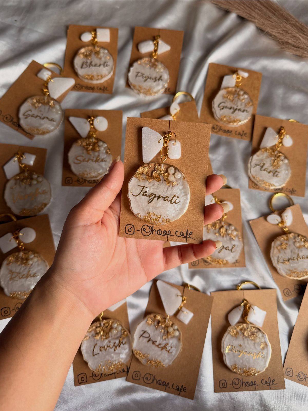 Hand holding a personalized white resin keychain with gold flakes and a name.